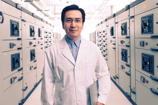 Technisches Personal in weißem Kittel lächelt während der Arbeit im Spannungsraum in die Kamera — Stockfoto