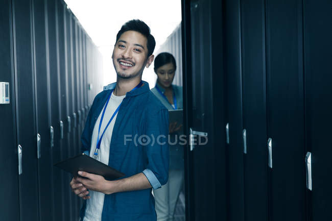 Чоловік працівник посміхається на камеру, в той час як інженер-жінка працює в кабінеті технічного обслуговування — стокове фото