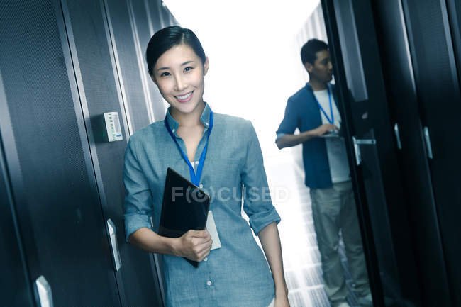 Женщина-работница улыбается в камеру, в то время как мужчина-инженер работает в комнате технического обслуживания — стоковое фото