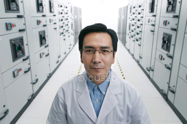 Personal técnico en bata de laboratorio sonriendo a la cámara mientras trabaja en la sala de voltaje - foto de stock