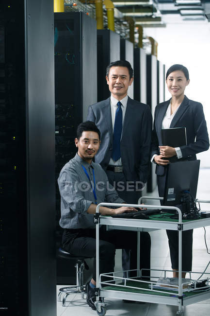 Технічний персонал, який використовує комп'ютер і посміхається на камеру під час роботи в кабінеті технічного обслуговування — стокове фото