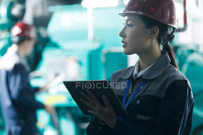 Female technician in helmet inspecting fire control in factory and looking away — Stock Photo