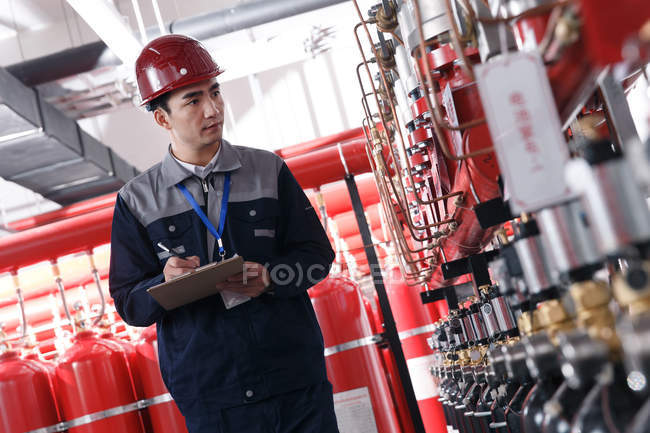 Ingeniero masculino profesional en el sombrero duro que trabaja en la inspección de la sala de control de incendios de fábrica - foto de stock