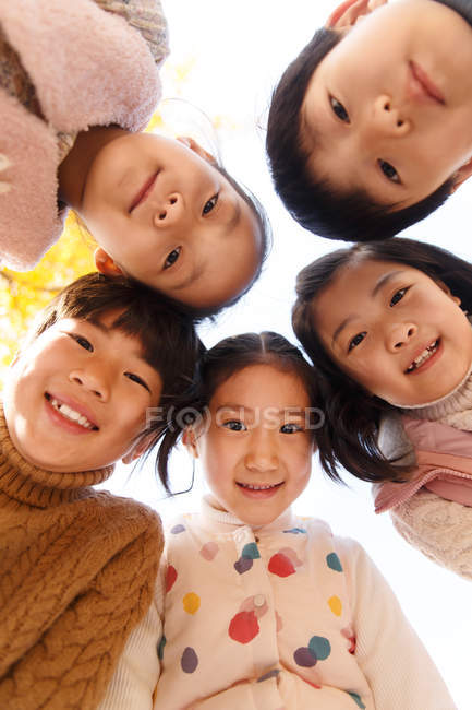 Low angle view of five adorable smiling asian kids looking at camera in autumnal park — Stock Photo