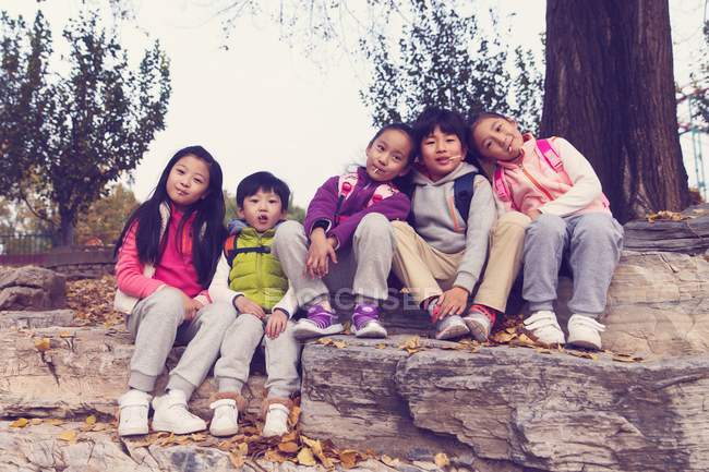 Cinque adorabile asiatico bambini seduta su pietre e guardando fotocamera in autunno parco — Foto stock