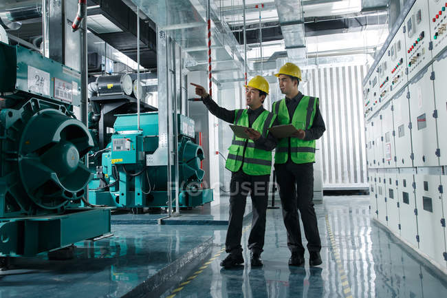 Engenheiros profissionais do sexo masculino em chapéus duros que trabalham na fábrica — Fotografia de Stock