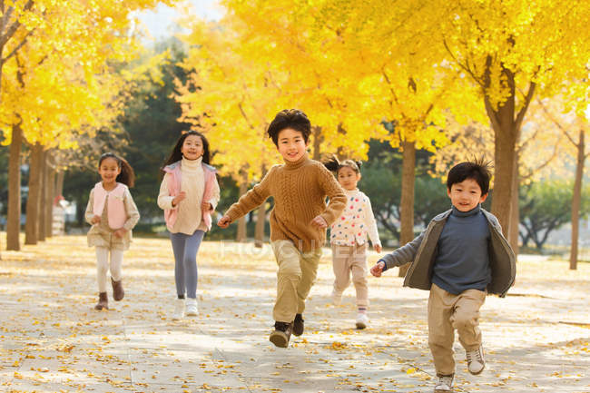 Happy five adorable asian kids running in autumnal park — Stock Photo