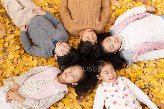 Vue grand angle de cinq adorables enfants asiatiques couchés sur le feuillage dans le parc automnal — Photo de stock