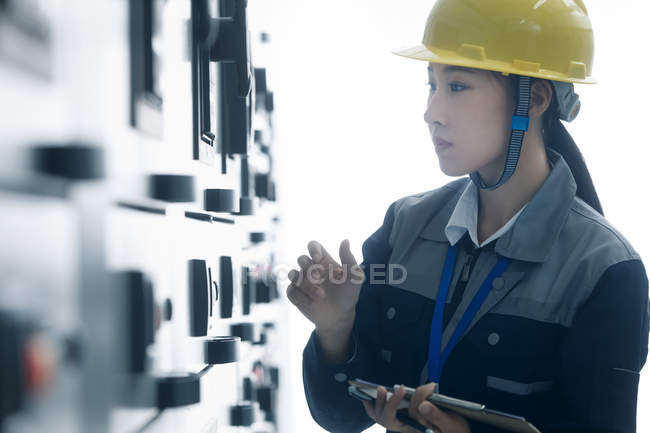 Técnico femenino en casco amarillo trabajando en fábrica - foto de stock