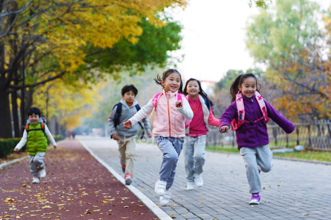 Five adorable asian kids running on road in autumnal park — Stock Photo