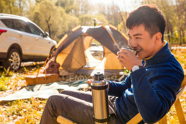 Handsome asian man drinking tea in autumnal forest — Stock Photo