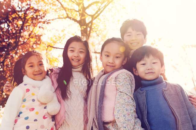 Fünf entzückende asiatische Kinder, die sich im herbstlichen Park umarmen und in die Kamera schauen — Stockfoto