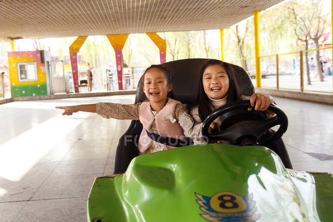 Niedliche fröhliche chinesische Mädchen fahren Auto und spielen zusammen auf dem Spielplatz — Stockfoto