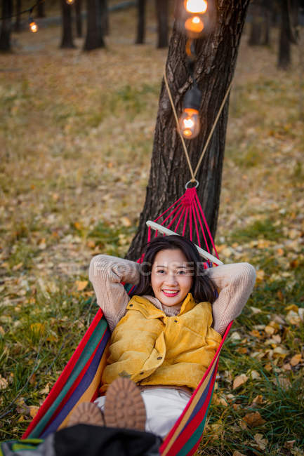 Ángulo alto vista de sonriente mujer asiática acostada en hamaca en bosque otoñal - foto de stock
