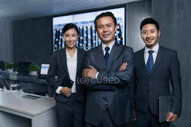 Professionelle Geschäftsleute lächeln in die Kamera, während sie gemeinsam im Kontrollraum arbeiten — Stockfoto