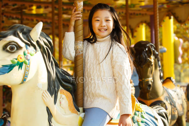 Adorable niña feliz jugando con carrusel y sonriendo a la cámara - foto de stock