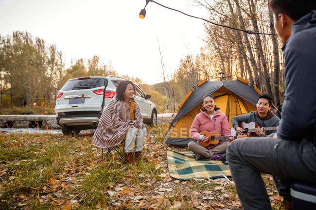 Asian friends playing guitar and ukulele at camping in autumnal forest — Stock Photo