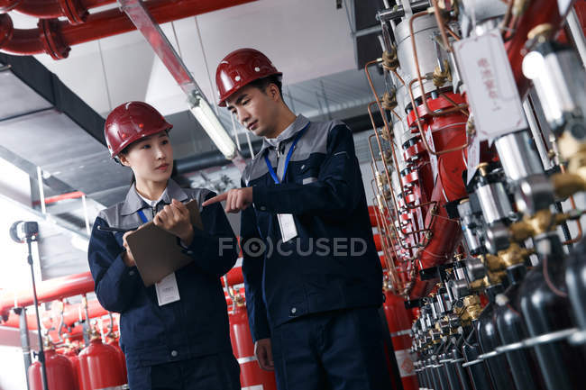 Ingenieros profesionales masculinos y femeninos en sombreros duros que trabajan en la inspección de la sala de control de incendios de fábrica - foto de stock