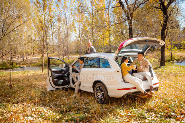Masculino e feminino ásia amigos sentado no carro no outonal floresta — Fotografia de Stock