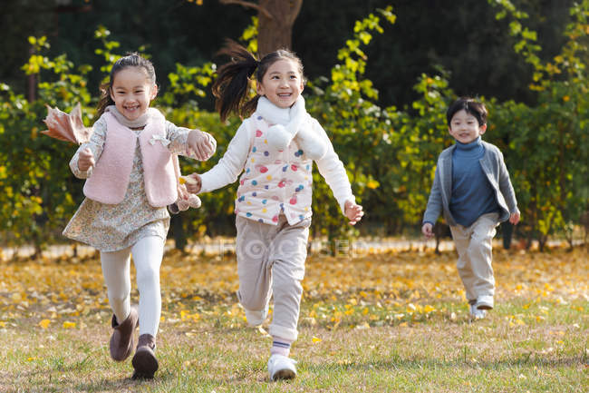 Happy kids playing together and running on meadow in autumn park — Stock Photo