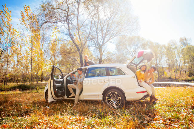 Male and female asian friends sitting in car in autumnal forest — Stock Photo