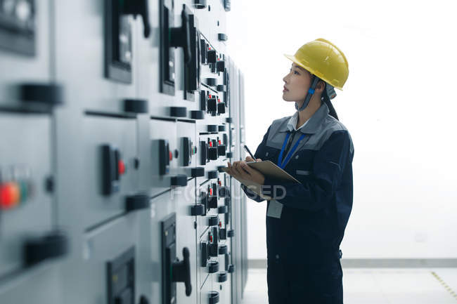 Female technician in yellow helmet working in factory — Stock Photo