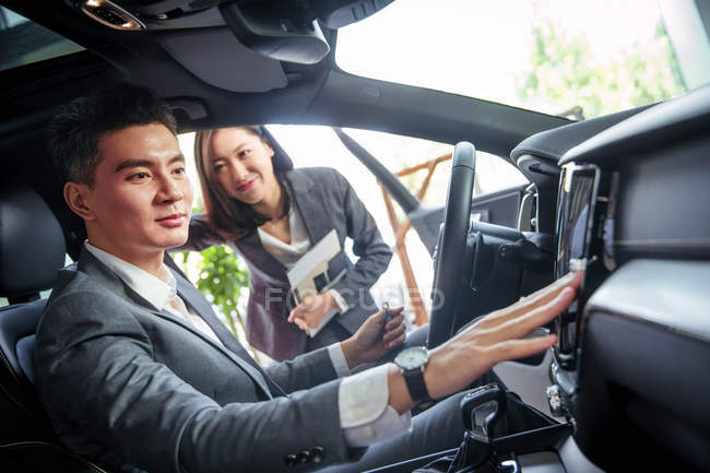 Азиатский бизнесмен покупает новый автомобиль и трогает кнопки в выставочном зале — стоковое фото