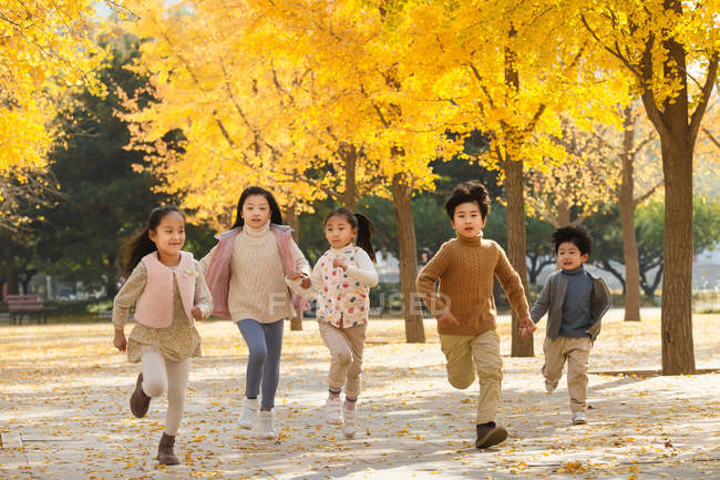 Five adorable asian kids running in autumnal park — Stock Photo