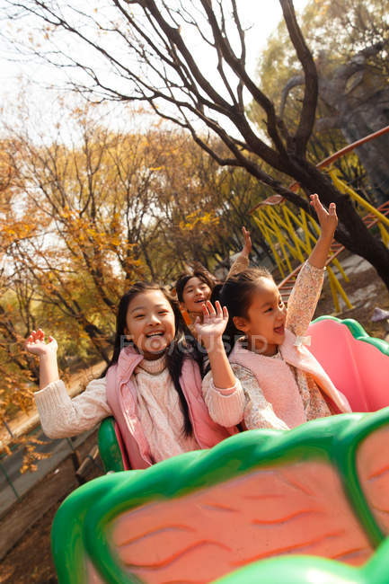 Happy asian children sitting together on roller coaster in park — Stock Photo