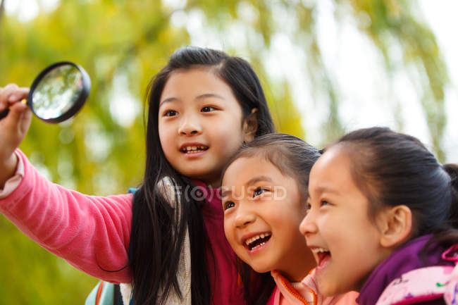 Três adorável asiático crianças abraçando e olhando para lupa no outonal parque — Fotografia de Stock