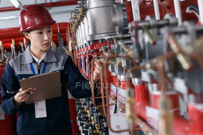 Женщина-техник в шлеме осматривает пожарный контроль на заводе — стоковое фото