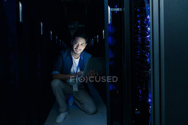 Технический персонал, работающий с компьютером и улыбающийся на камеру в комнате технического обслуживания — стоковое фото