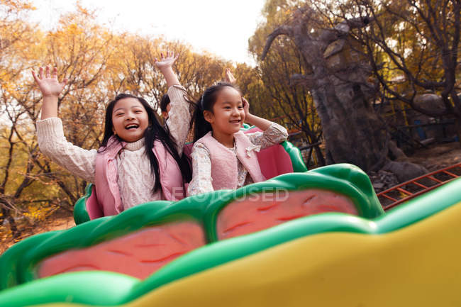 Happy boy and girls sitting together on roller coaster in park — Stock Photo