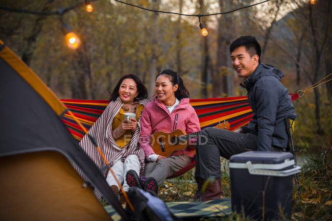 Lächelnde asiatische Freunde mit Ukulele auf Hängematte im herbstlichen Wald — Stockfoto