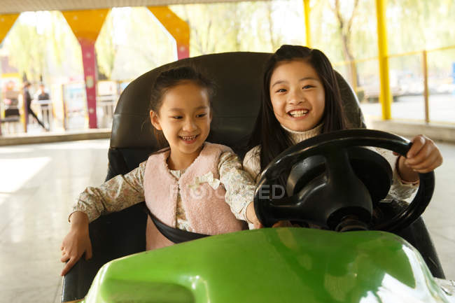 Bonito alegre chinês meninas equitação carro e jogar juntos no playground — Fotografia de Stock