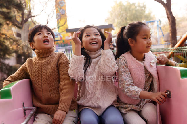 Happy boy and girls sitting together on roller coaster in park — Stock Photo