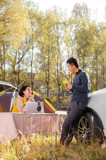 Asiatisches Paar schaut sich auf Zeltplatz im herbstlichen Wald an — Stockfoto