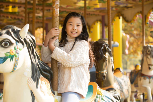 Adorable happy little girl playing with carousel and smiling at camera — Stock Photo
