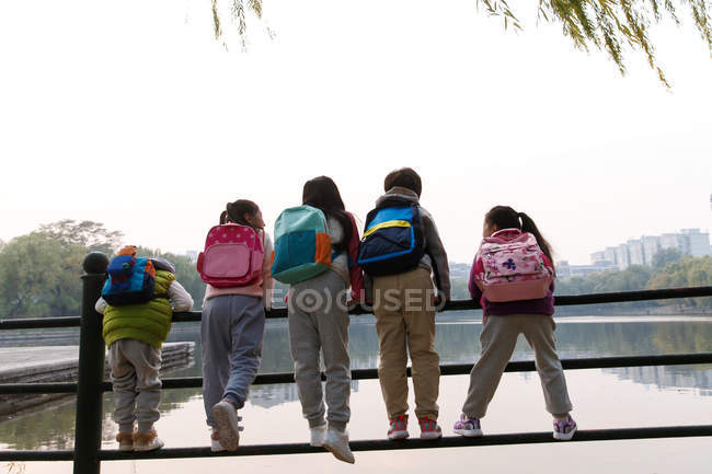 Back view of five kids leaning on fence near river in autumnal park — Stock Photo