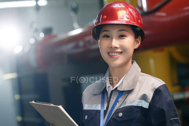 Sorridente técnica feminina no capacete inspecionando o controle de incêndio na fábrica e olhando para a câmera — Fotografia de Stock