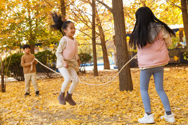 Ragazzo felice e ragazze che giocano insieme e saltano nel parco autunnale — Foto stock