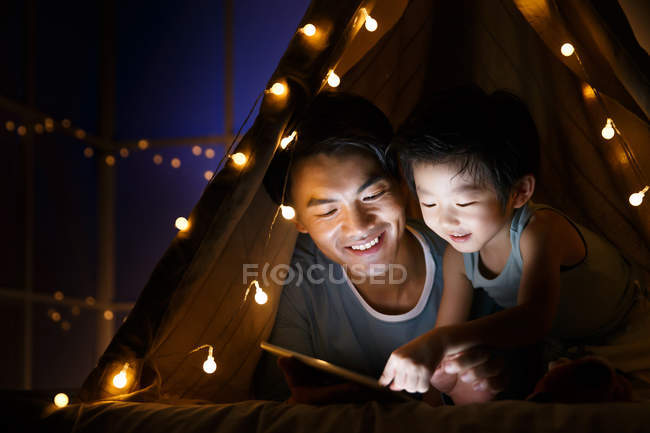 Happy asian father and preschooler son watching something on tablet in tent at home — Stock Photo