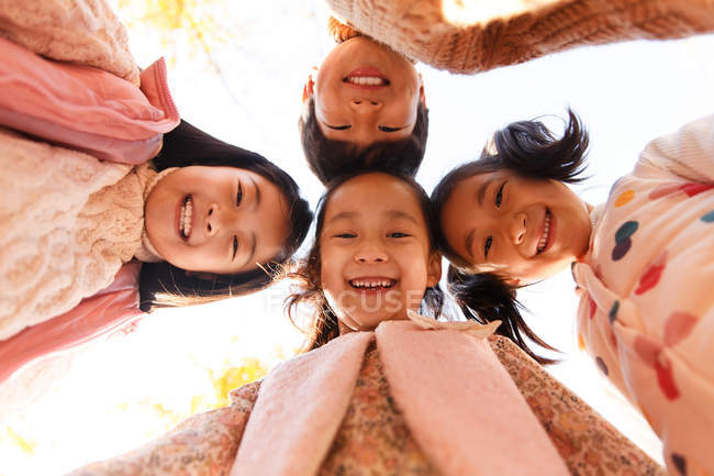 Niños felices de pie juntos y sonriendo a la cámara en el parque de otoño, vista de bajo ángulo - foto de stock