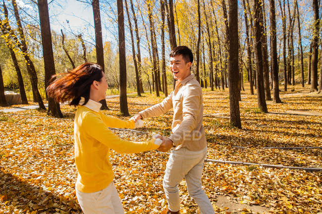 Feliz asiática pareja cogida de la mano y bailando en otoñal bosque - foto de stock