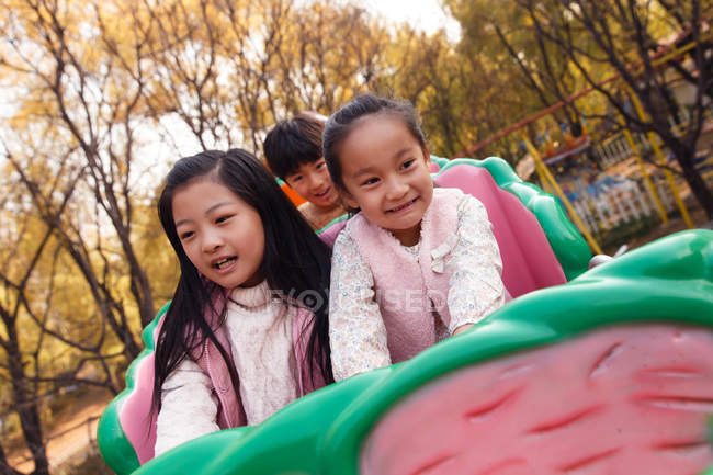 Счастливые мальчики и девочки, играющие вместе на горках в парке — стоковое фото