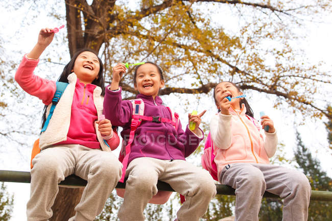 Vue à faible angle de trois adorables enfants asiatiques soufflant des bulles de savon dans le parc automnal — Photo de stock