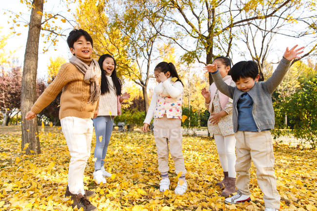 Cinco adorável asiático crianças brincando com amarelo folhas no outonal parque — Fotografia de Stock