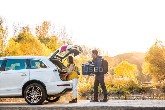 Asian couple taking stuff for picnic from car in autumnal forest — Stock Photo
