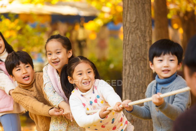 Fünf entzückende glückliche asiatische Kinder, die im herbstlichen Park gemeinsam Seil ziehen — Stockfoto
