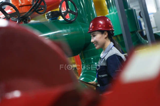 Sorridente tecnico donna in casco che ispeziona il controllo del fuoco in fabbrica — Foto stock